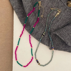 Detail of colorful natural stone beaded necklaces with gold clasps on grey knit fabric