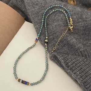 Detail of beaded necklace with teal crystals and gold clasp on a grey knit texture