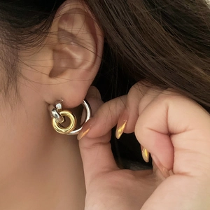 Close-up of interlocking gold and silver geometric hoop earrings on a female model