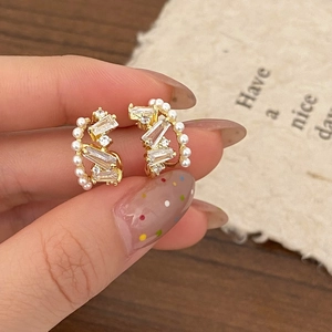 Detailed close-up of gold pearl earrings with zircon stones shown in hand display