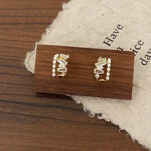 Detail of C-shaped gold earrings featuring lustrous pearls and baguette-cut zircons