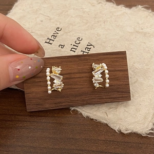 Elegant gold zircon pearl hoop earrings displayed on a dark wooden block stand