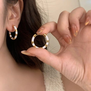 Gros plan de créoles françaises en émail or et blanc avec un motif à rayures chic