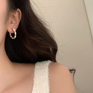 Gros plan d'une boucle d'oreille créole française en métal doré et émail blanc