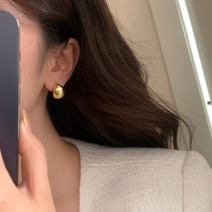 Close-up of gold brushed metal teardrop earrings on model with white tweed jacket