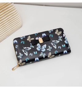 Détail du portefeuille noir à motifs papillons avec nœud doré et fermeture éclair élégante
