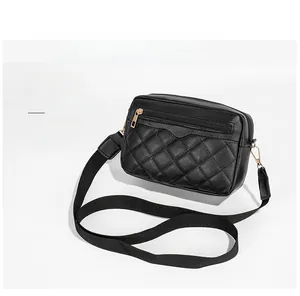 Detail of black quilted crossbody camera bag with golden zippers and wide textile strap