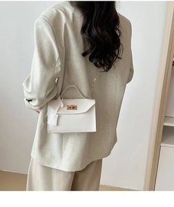 Detail view of white chain strap handbag with gold twist lock on a neutral background