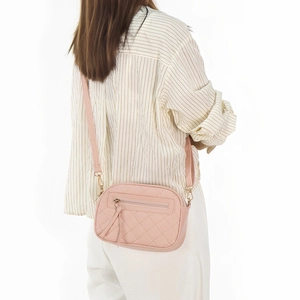 Pink quilted crossbody bag with triple zippers and tassel detail shown on model