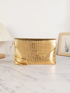 Close-up of gold envelope handbag with crocodile pattern and stylish wrist strap