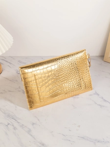 Detail of golden crocodile pattern hand-held clutch on marble surface with soft lamp light