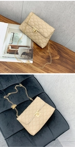 Detail der beigen Stepptasche mit goldenem Drehverschluss und Kettenriemen auf Holz