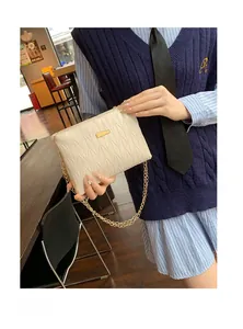 Detail of a beige quilted crossbody bag with golden chain and metallic logo plate