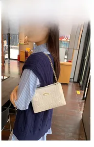 Detail of off-white quilted crossbody bag with gold metal clasp and elegant chain strap