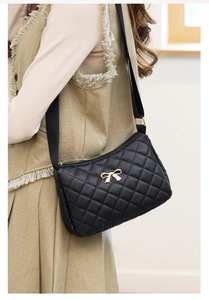 Detail of black quilted shoulder bag featuring a gold metal bow and woven wide strap