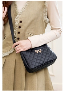 Detail of black quilted crossbody bag with golden metal bow and leather strap decoration