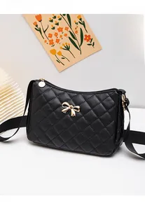 Detail of black quilted crossbody bag with golden metal bow and adjustable wide strap