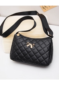 Close-up of black quilted shoulder bag featuring a decorative golden metal bow accent