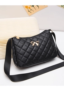 Detail of black quilted shoulder bag featuring gold bow accent and zip texture