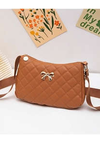 Detail of caramel brown quilted crossbody bag featuring a golden metal bow and woven strap