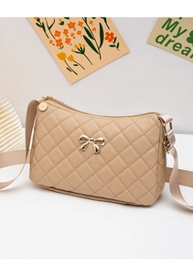 Detail of beige quilted shoulder bag featuring a golden metal bow and woven wide strap