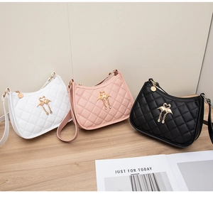 Détail de trois sacs portés épaule matelassés en blanc, rose et noir avec pompons