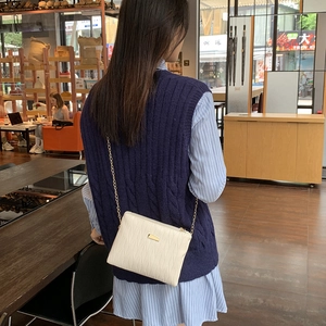 White quilted crossbody bag with gold chain strap worn by a model in a cafe setting