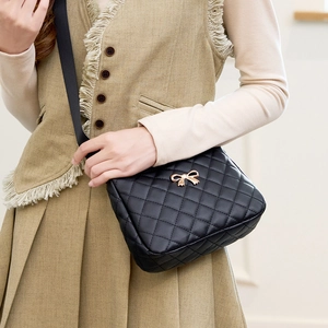 Classic black quilted crossbody bag with golden bow accessory worn by a model