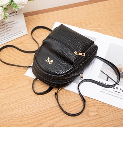 Detail of a black crocodile pattern mini backpack with a golden bow on a wood floor