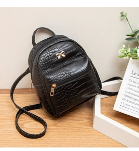 Detail of a mini black crocodile pattern backpack with a gold bow accent on wood background