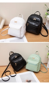 Detail view of mini crocodile texture backpacks with golden bow accents in white and green