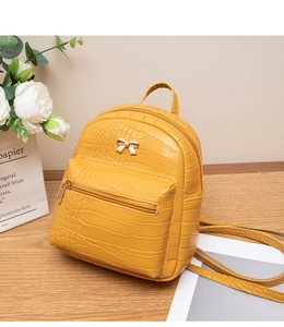 Detail of yellow crocodile pattern mini backpack with gold bow and floral decoration