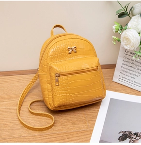 Detail of yellow crocodile pattern mini backpack with golden bow and leather texture