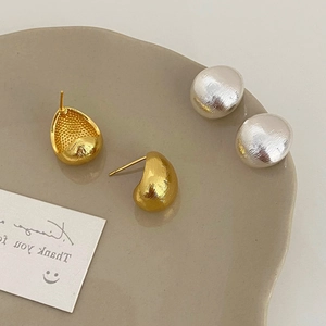 Brushed metal teardrop stud earrings in gold and silver finish on ceramic tray