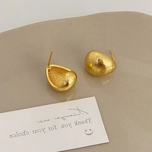 Detailed view of golden brushed metal teardrop earrings on a ceramic display tray