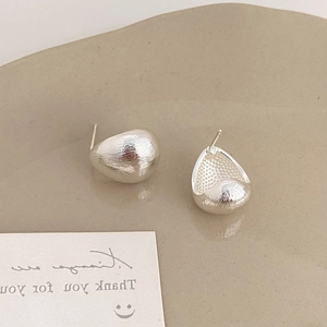 Macro detail of silver teardrop earrings with brushed metal finish on a ceramic plate