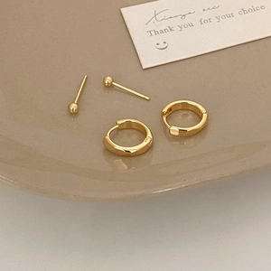 Detailed view of polished minimalist gold hoop earrings and ball studs set on ceramic