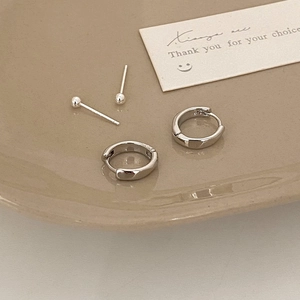 Close-up of silver hoop earrings and ball studs set on minimalist ceramic tray