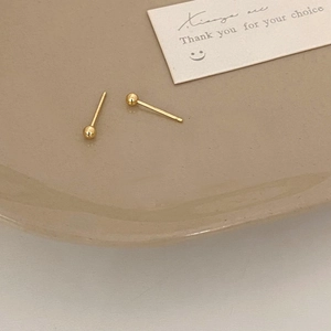Detailed view of polished golden round stud earrings on a minimalist ceramic tray