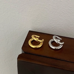 Detail of minimalist gold and silver double-layered ear cuffs on a dark wood stand