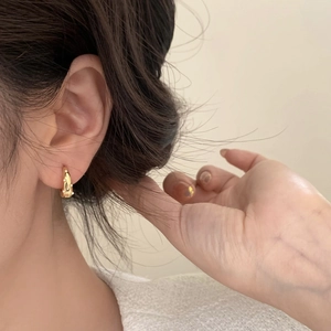 Close-up of golden hoop earrings with small white pearls worn on a model's ear