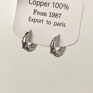 Detail of silver-colored copper hoop earrings with small round bead studs on a white card