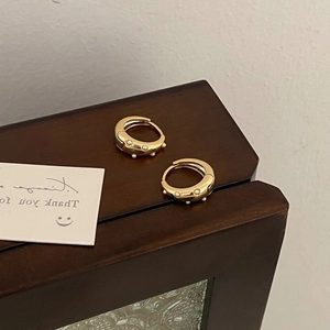 Detailed close-up of vintage gold hoop earrings with small pearls on a wooden frame