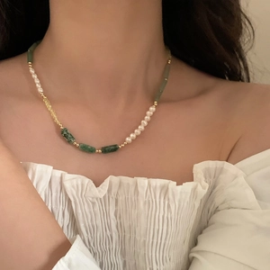 Bamboo style necklace with freshwater pearls and green stones on model collarbone