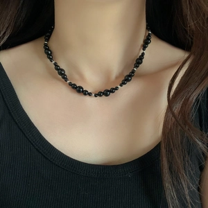 Collier minimaliste en perles noires et entretoises argentées porté pour un look moderne