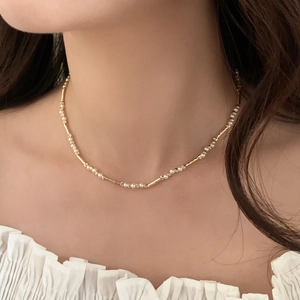 Detail einer eleganten Goldhalskette mit weißen Perlen und Zylindern am Frauenhals