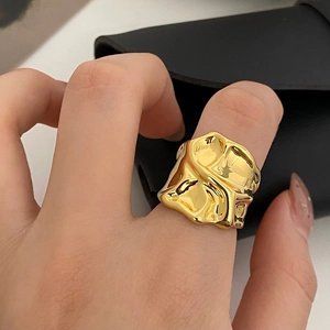 Close-up of wide gold ring with irregular wrinkled texture on a female model finger