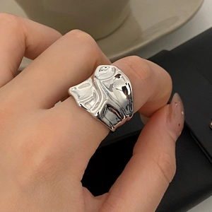 Macro shot of silver irregular lava texture wide band ring on hand with elegant props