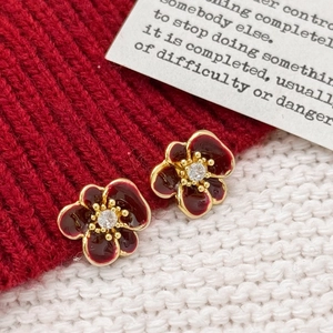 Close-up of burgundy flower earrings with gold edges and zircon center on knit fabric