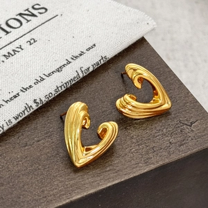 Macro detail of abstract heart-shaped gold-plated stud earrings on a vintage fabric bag